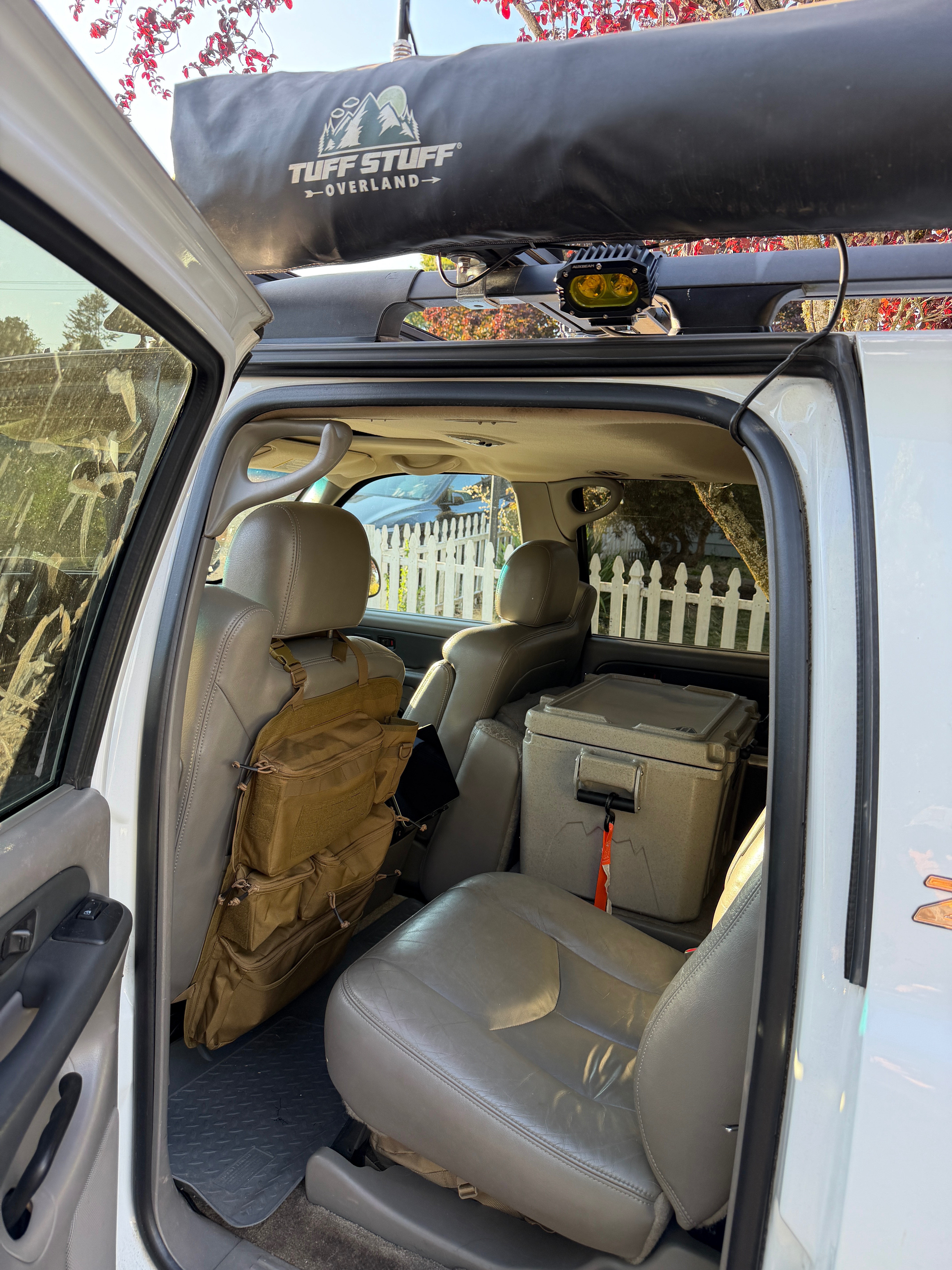 Coyote tan MOLLE seat back organizer and hard cooler loaded in the second row of a GMT800 Suburban with a rooftop awning