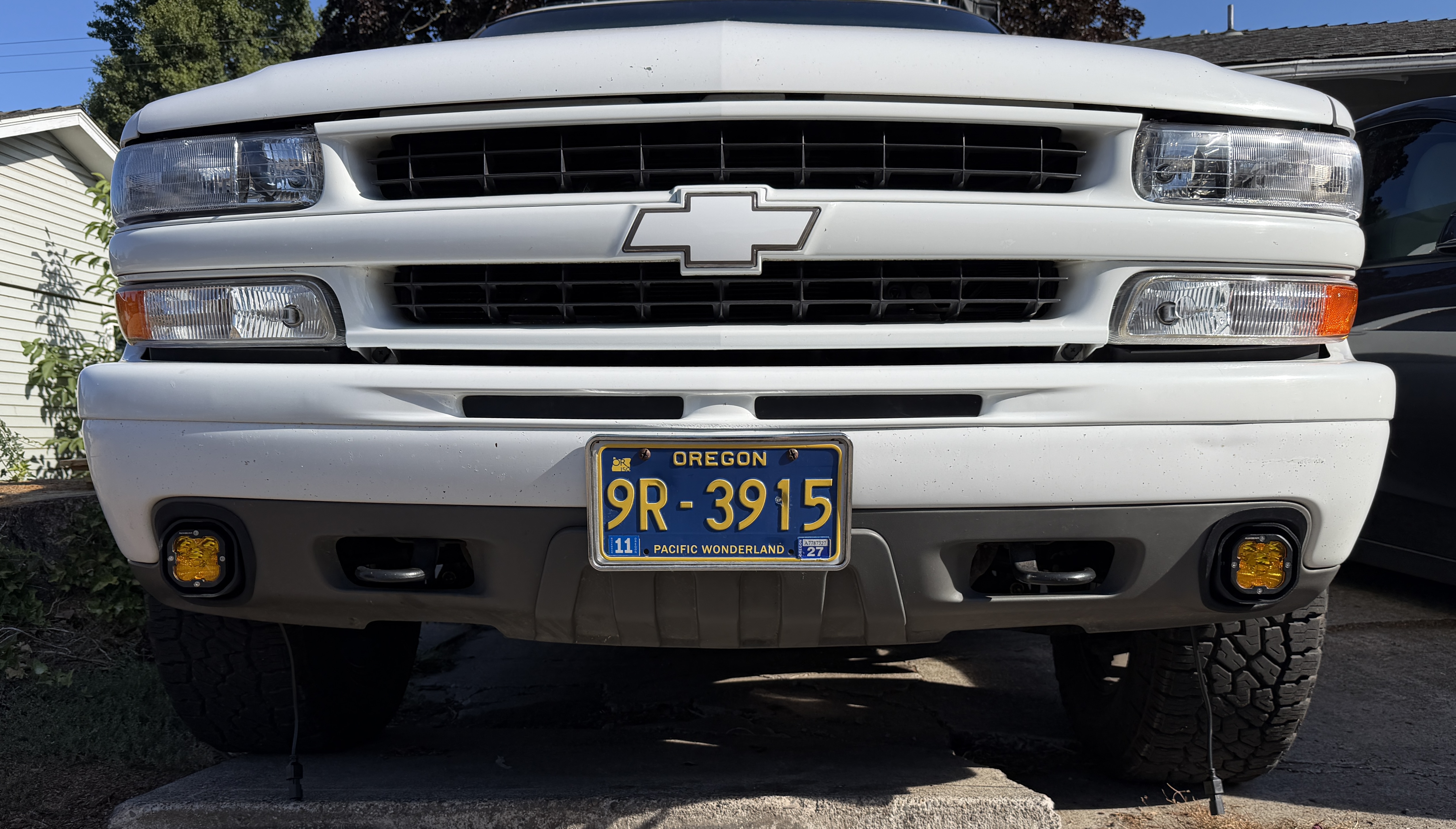 Front grille of the white Suburban Z71 with amber square fog lights in the lower bumper corners and a Chevy bowtie graphic wrap