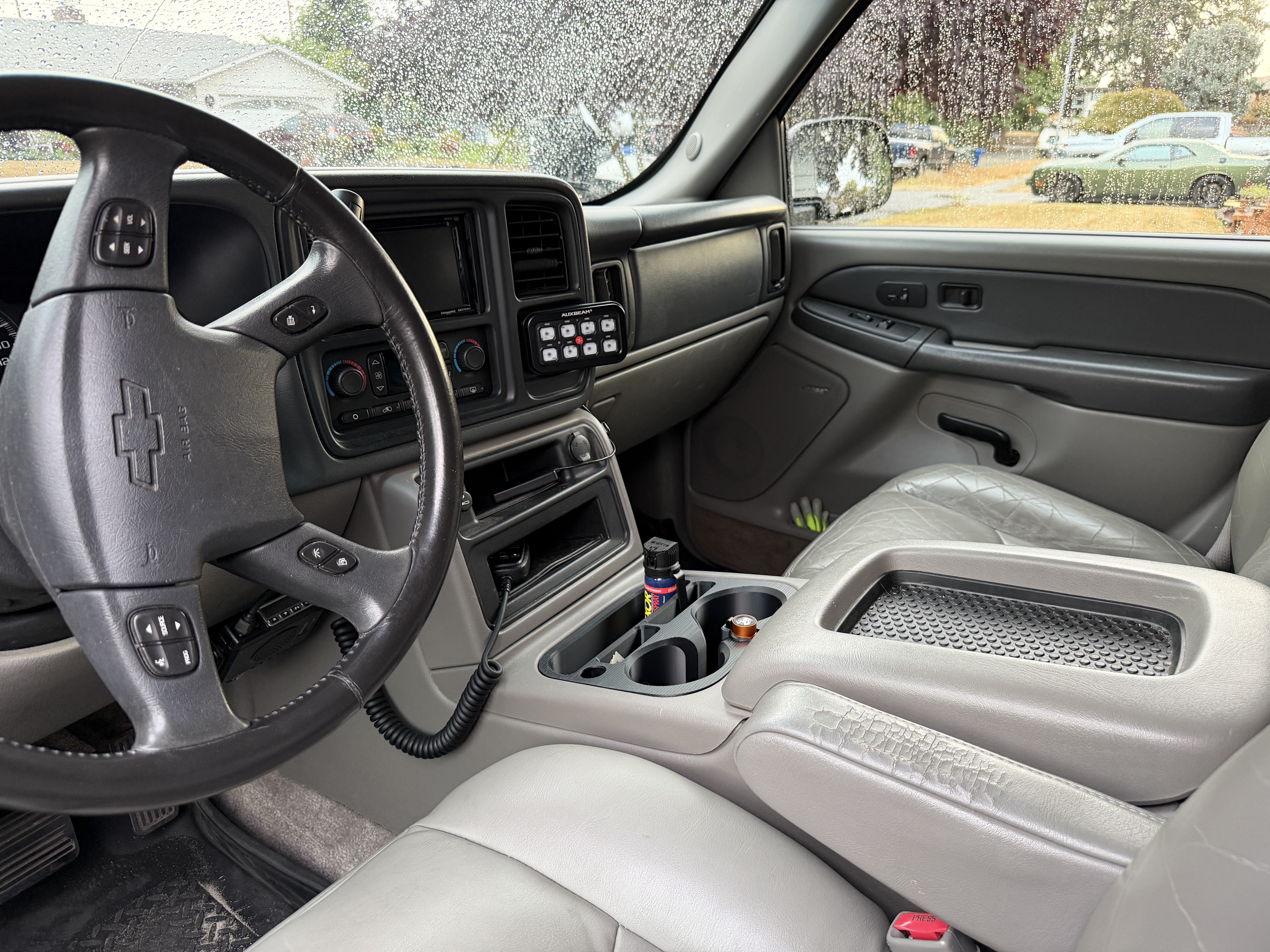 Front cabin of the Suburban with an Auxbeam switch panel mounted in the dash cubby and an Olight flashlight in a custom cup holder mount