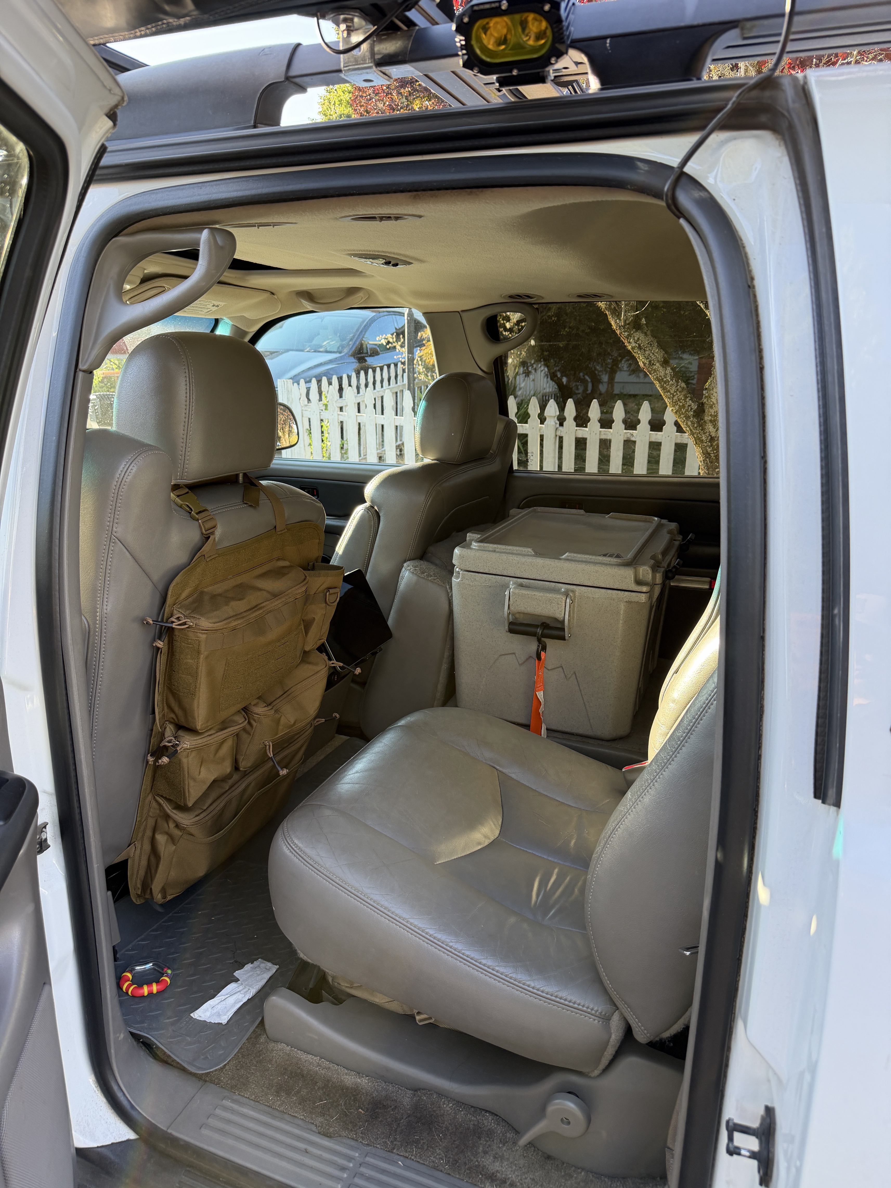 Middle row of the Suburban with a coyote MOLLE seat-back gear bag and tablet mount, and a tan Cordova cooler strapped to a folded seat