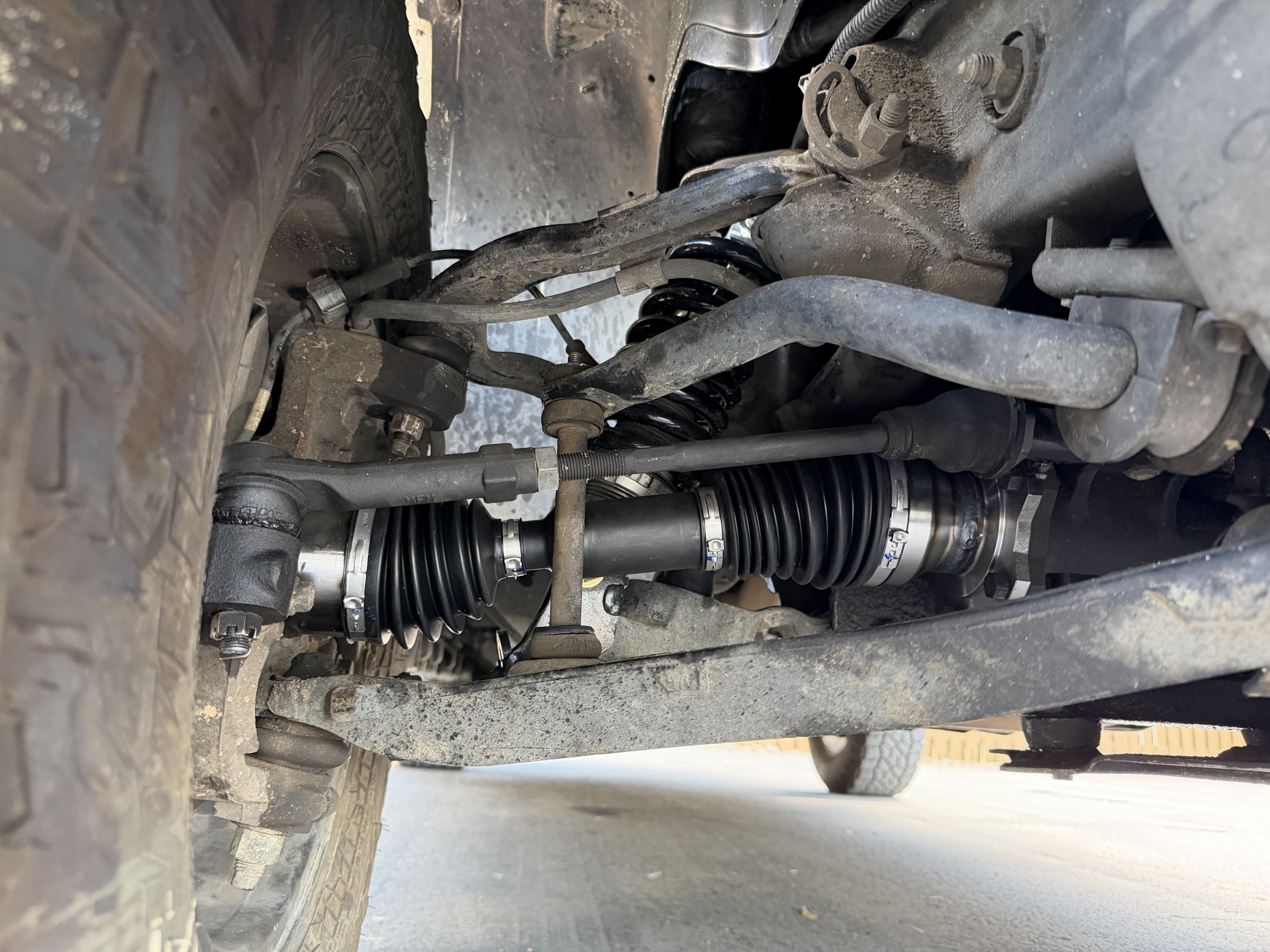 Underbody view of the Suburban's front suspension showing the Viking coilover, Trackmotive CV axle with fresh boots, tie rod, and sway bar
