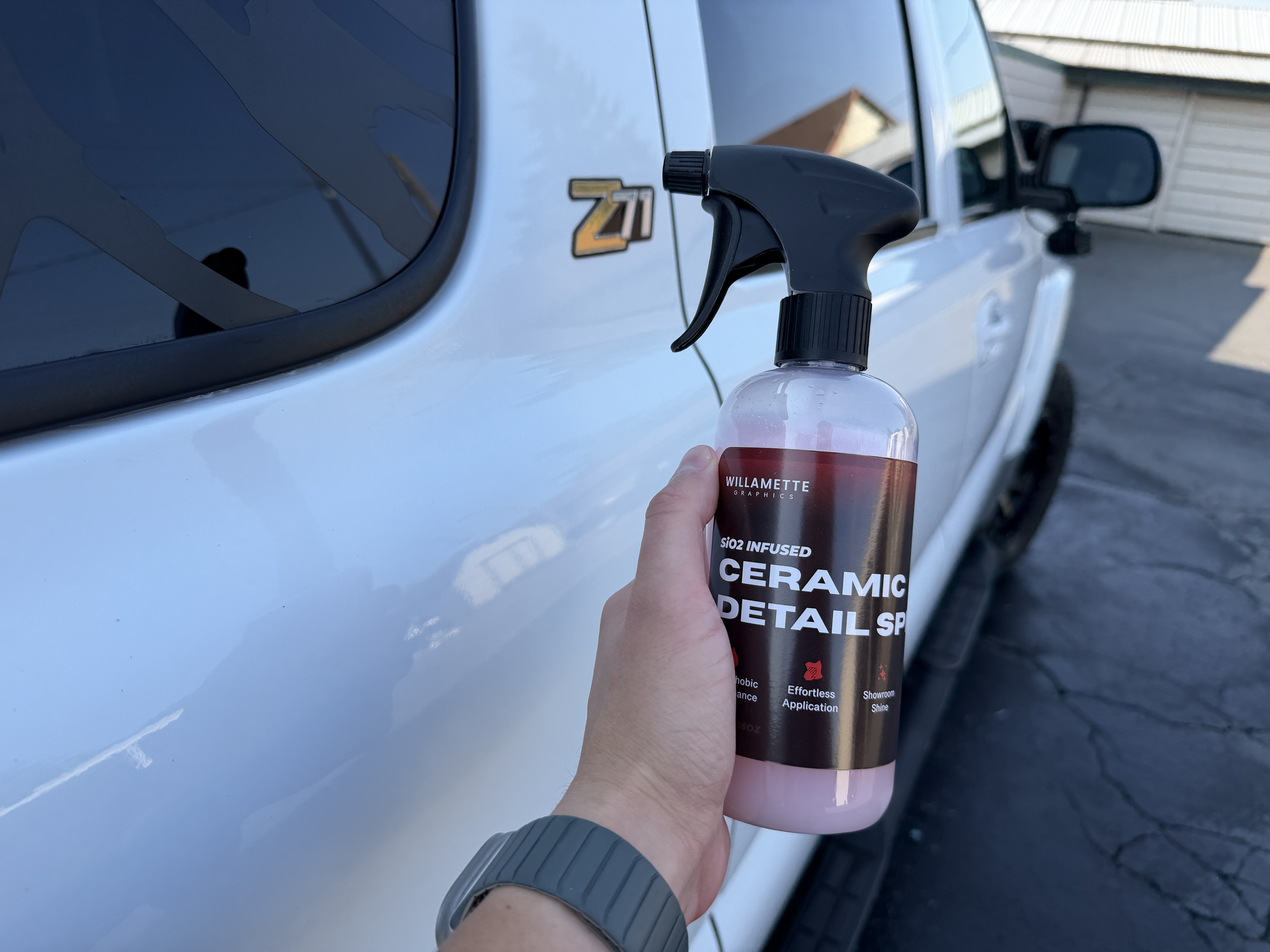 Hand holding a Willamette Graphics SiO2 Infused Ceramic Detail Spray bottle beside a glossy white Z71 door